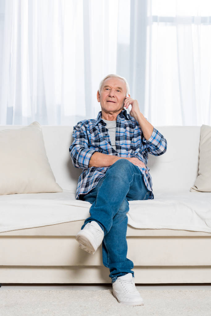 senior man talking on smartphone while sitting on sofa at home - Photo, Image
