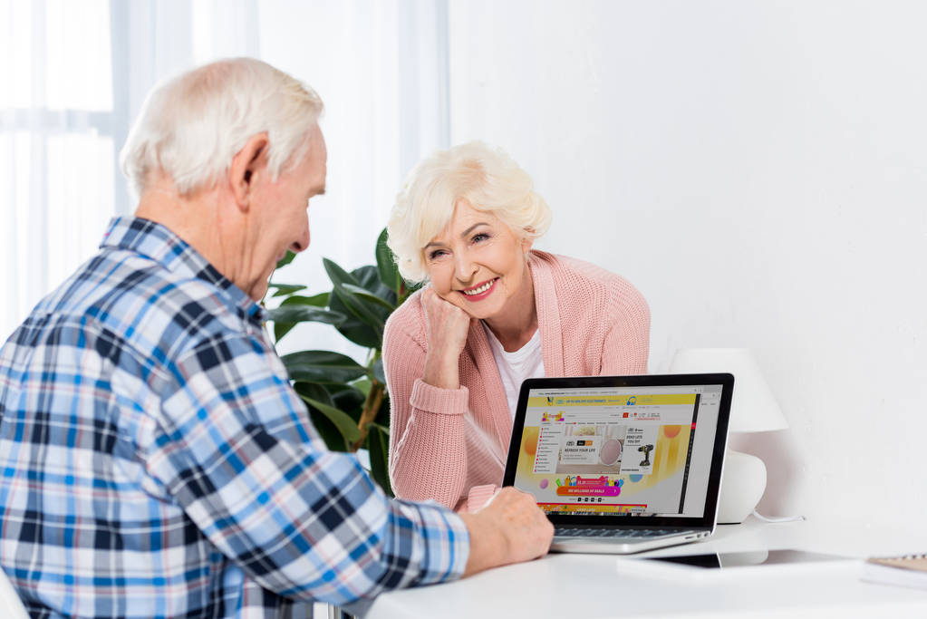 ritratto di donna anziana che guarda il marito usando il computer portatile con logo aliexpress a casa
 - Foto, immagini