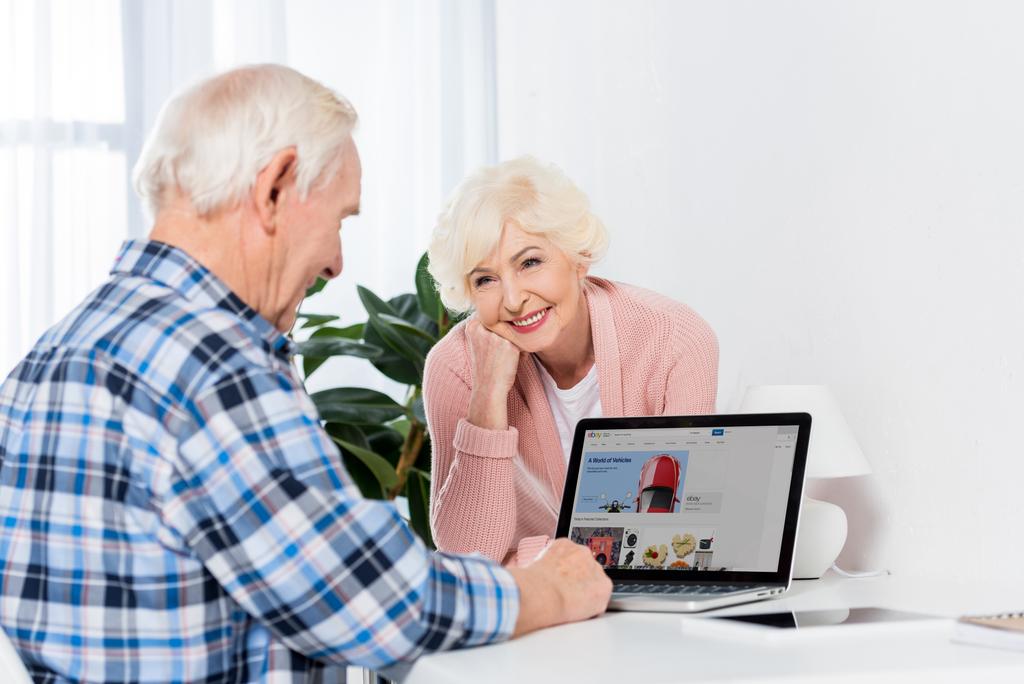 портрет старшого жінки, дивлячись на чоловіка, використовуючи ноутбук з ebay логотип на дому - Фото, зображення