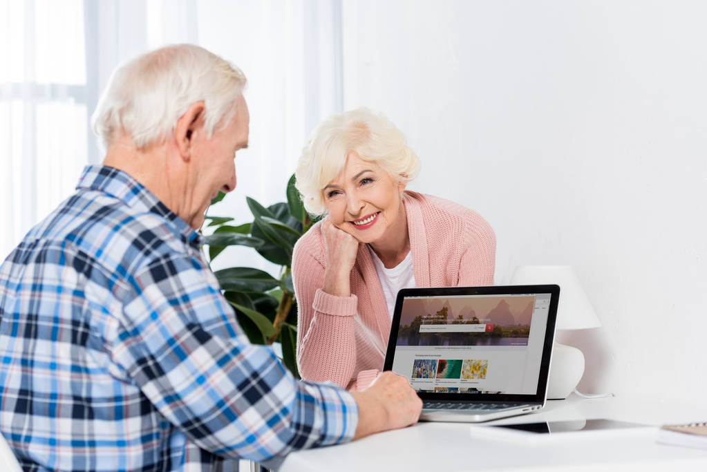 自宅のノート パソコンを使用しての夫を見て満足している年配の女性の肖像画 - 写真・画像