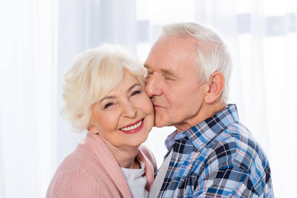 muotokuva vanhempi mies suutelee onnellinen vaimo, joka katselee kameraa
 - Valokuva, kuva