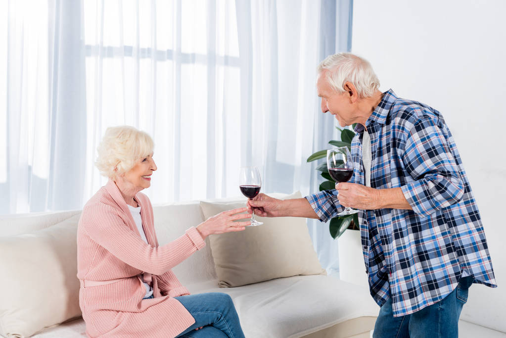 Widok z boku starszego człowieka dając kieliszek czerwonego wina, żona w domu - Zdjęcie, obraz