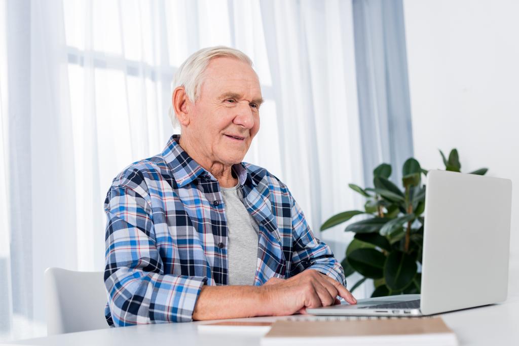 retrato del hombre mayor sentado en la mesa y usando el ordenador portátil en casa
 - Foto, imagen