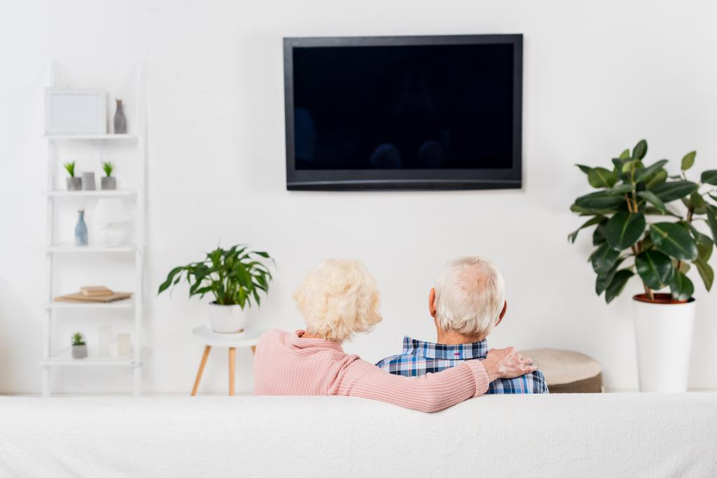 visão traseira do casal sênior assistindo tv e abraçando no sofá
 - Foto, Imagem