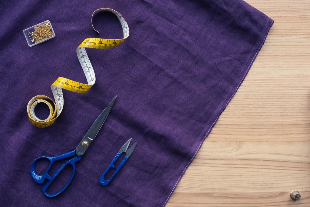 вид сверху на фиолетовую ткань с швейными инструментами на столе
 - Фото, изображение