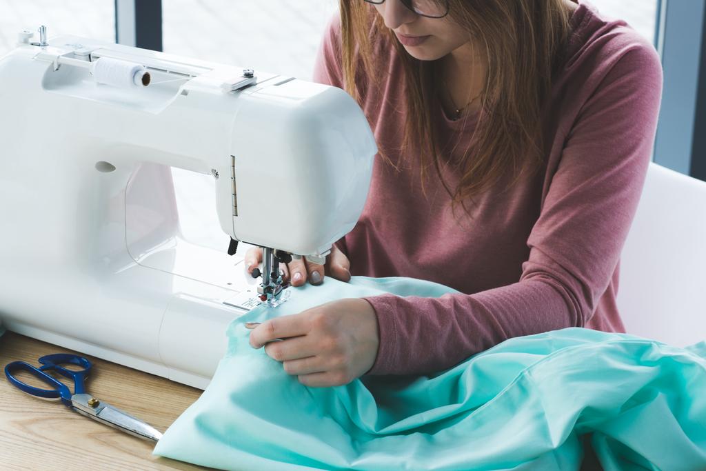 職場でミシンを使用して若い女性の裁縫師の画像をトリミング - 写真・画像