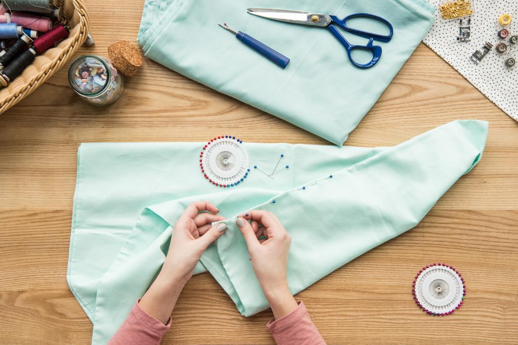 vista superior do tecido de costura de mãos femininas cortadas com agulha no local de trabalho de costureira
 - Foto, Imagem