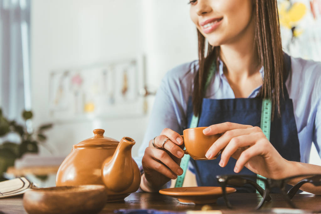 περικομμένη εικόνα μοδίστρα πίνοντας τσάι κατά τη διάρκεια γεύματος - Φωτογραφία, εικόνα