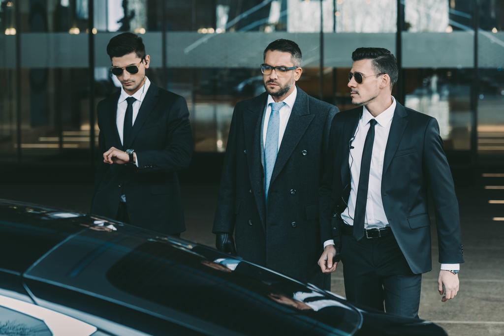 twee bodyguards gonna zwarte auto met zakenman - Foto, afbeelding