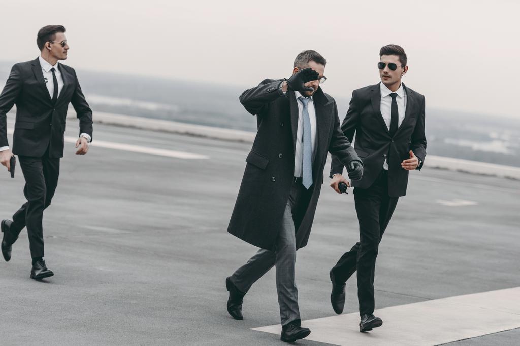 podnikatel, zakrývaje si tvář rukou a chůzi s bodyguardy na helipad - Fotografie, Obrázek