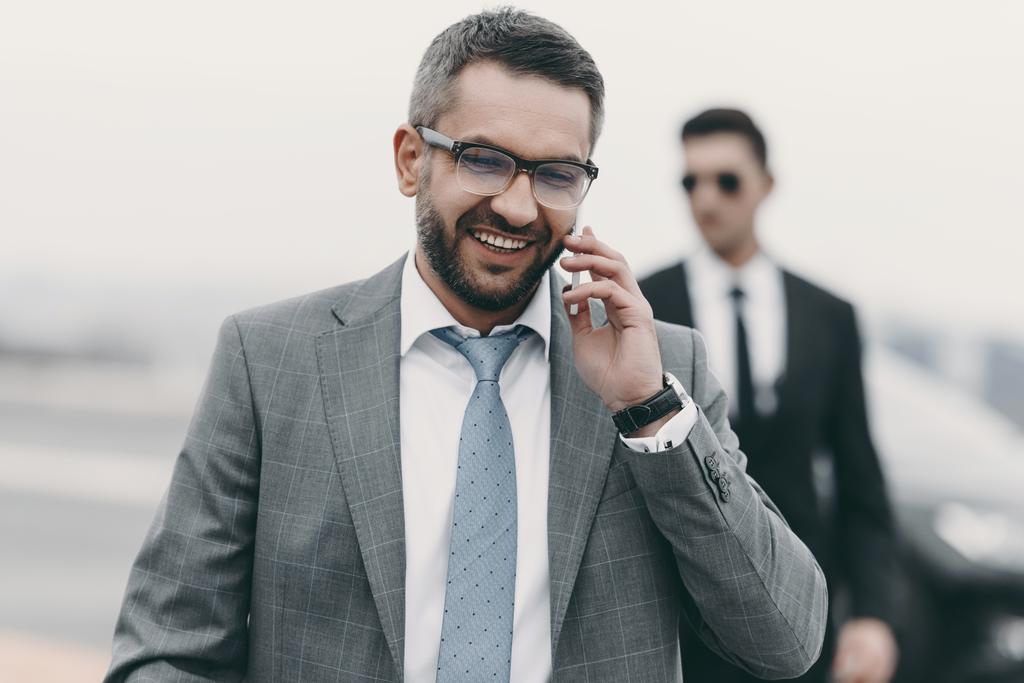 lachende zakenman met bodyguard praten door smartphone - Foto, afbeelding