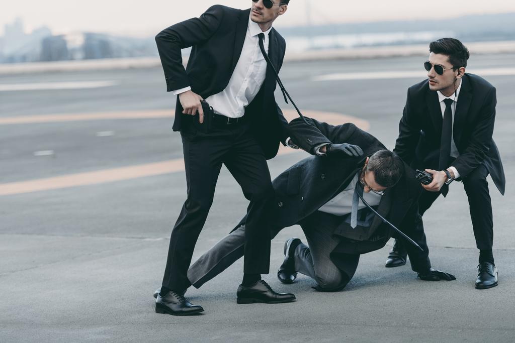 обрезанный образ двух телохранителей, защищающих падающего бизнесмена
   - Фото, изображение