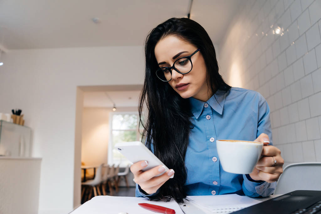 занятая успешная деловая женщина работает в кафе, пьет кофе, держит смартфон
 - Фото, изображение