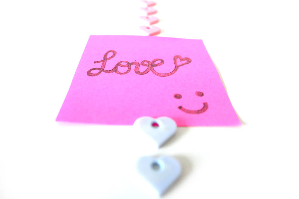 gezeichnetes Lächeln Gesicht mit Liebeswort auf rosa Aufkleberpapier Notiz auf weißem Hintergrund ideal für jeden Einsatz. - Foto, Bild