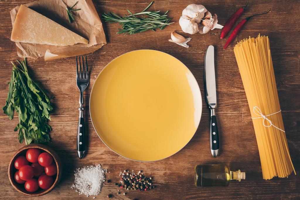 pohled shora řádku těstoviny, čerstvé suroviny a deska s nožem a vidličkou na dřevěný stůl - Fotografie, Obrázek