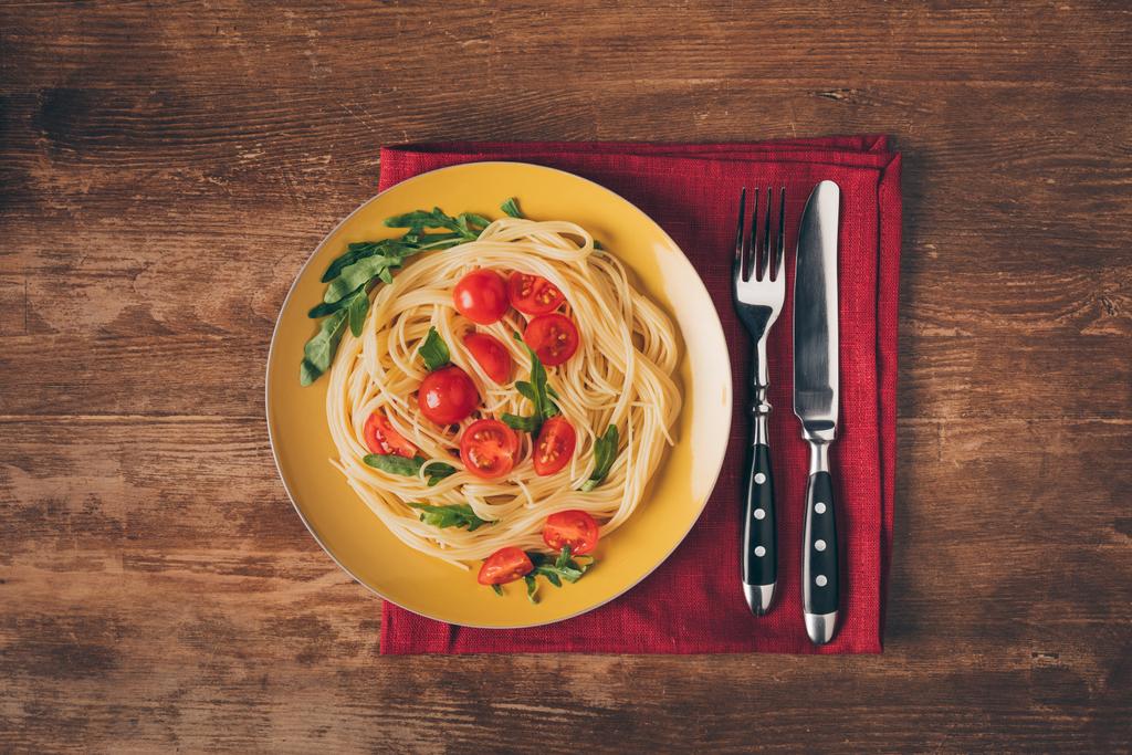 traditional italian pasta with tomatoes and arugula in plate with knife and fork on wooden tabletop - Photo, Image