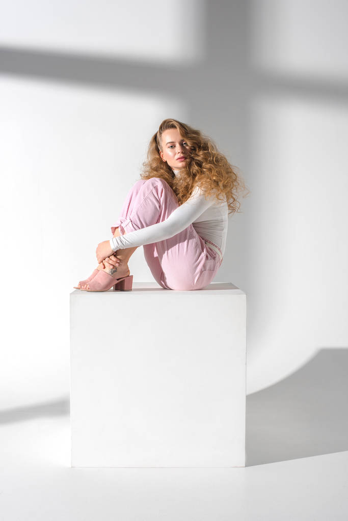 kaunis vakava nainen kihara tukka istuu valkoinen kuutio ja halaus jalat
 - Valokuva, kuva