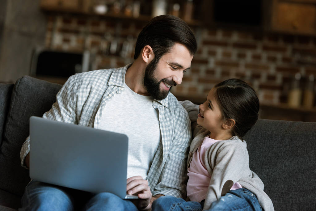vrolijke vader met dochter zittend op de Bank en het gebruik van laptop - Foto, afbeelding