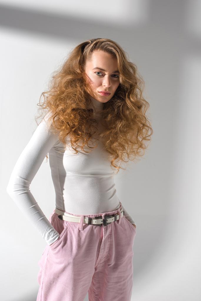 αυτοπεποίθηση κομψό κορίτσι με σγουρά μαλλιά στέκεται με τα χέρια στις τσέπες και βλέπουν τα φωτογραφικών μηχανών - Φωτογραφία, εικόνα
