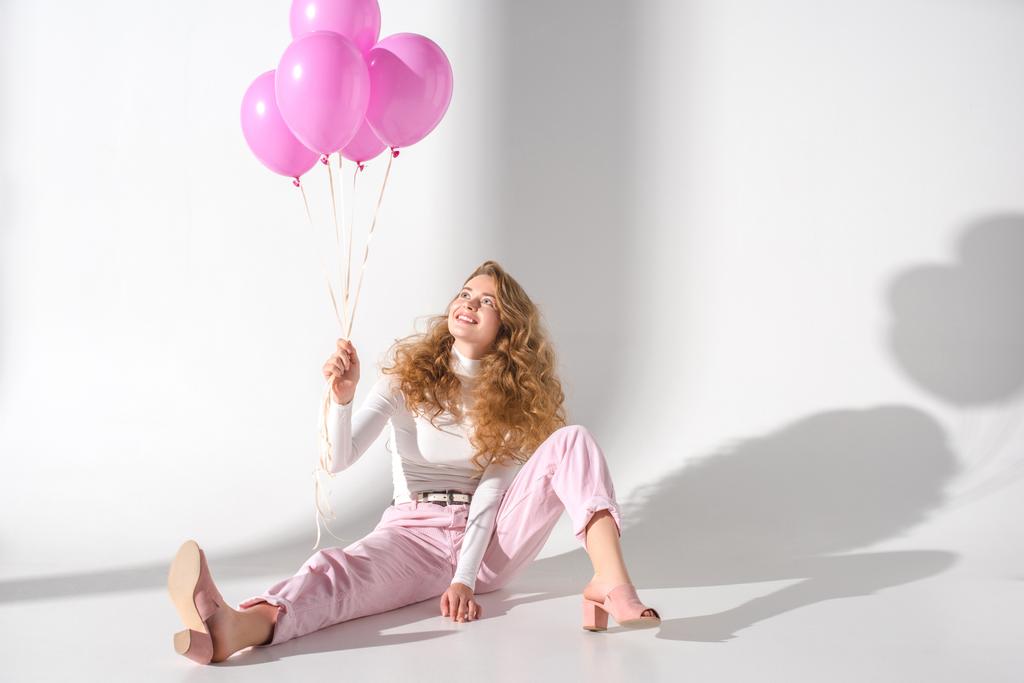 sonriente chica con paquete de globos de color rosa sentado y mirando hacia arriba
 - Foto, imagen