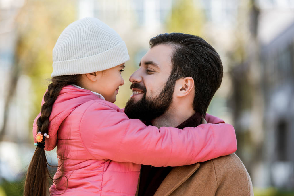 Gelukkig vader met dochter knuffelen in herfst-outfit en kijken naar elkaar. buiten - Foto, afbeelding