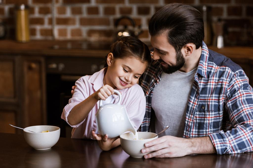 pai e filha derramando leite em tigela com lanches na cozinha
 - Foto, Imagem