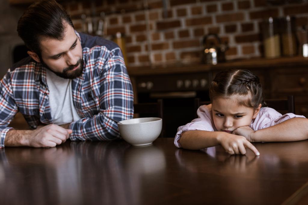 father with daughter sitting at table, little kid dont want eat breakfast at kitchen - Photo, Image