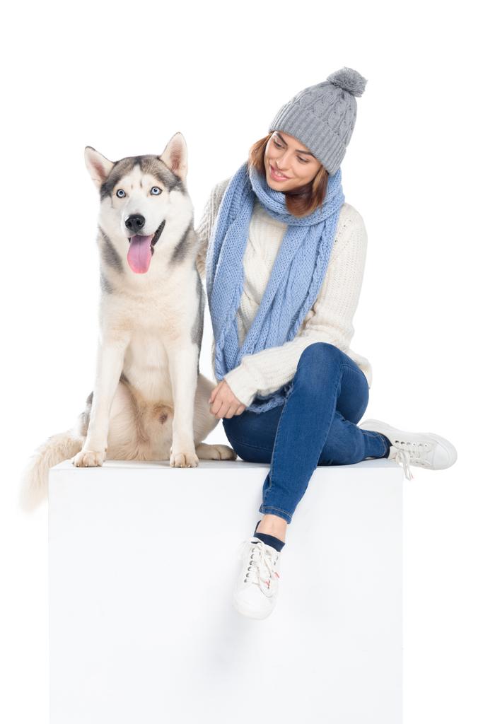 husky dog and woman in knitted hat and scarf sitting on white cube, isolated on white - Photo, Image