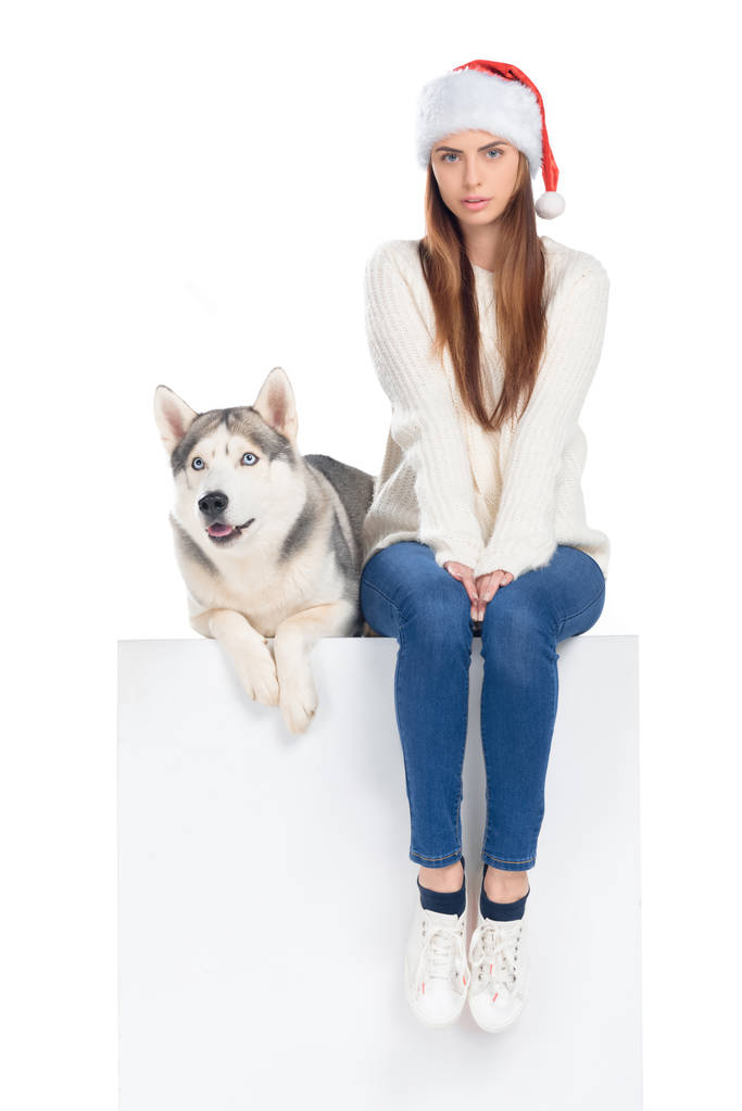 husky dog and beautiful woman in santa hat sitting on white cube, isolated on white - Photo, Image