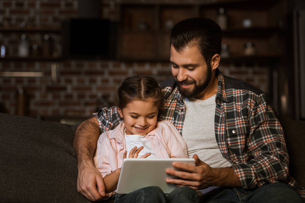 szczęśliwy ojciec z córką, siedząc na kanapie i za pomocą tabletu - Zdjęcie, obraz