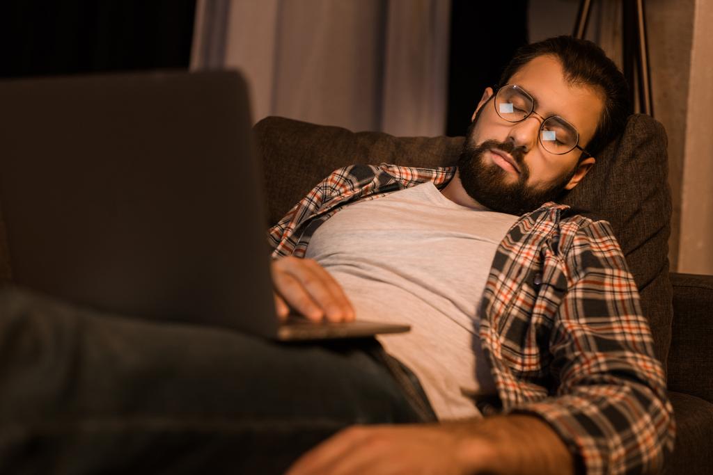 Müder Mann mit Brille sitzt auf Couch mit Laptop - Foto, Bild