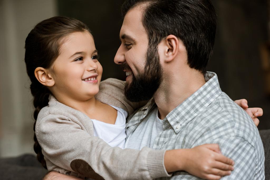 cheerful father and daughter hugging and looking at each other at home - Photo, Image
