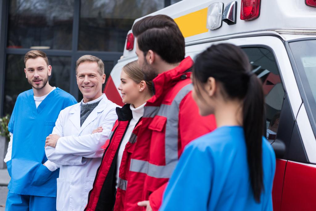 equipo de trabajo de paramédicos de pie delante del coche y mirándose
 - Foto, imagen