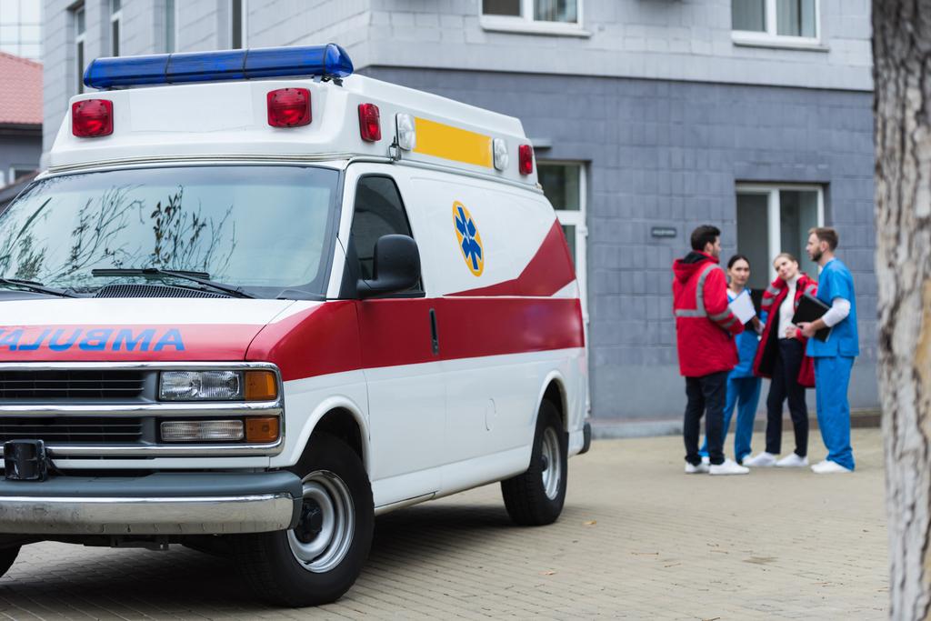 Vier ambulance artsen praten en staan in de buurt van auto - Foto, afbeelding