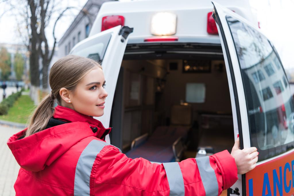 Genç kadın doktor ambulans kapılarını açıyor ve uzağa arıyorsunuz - Fotoğraf, Görsel