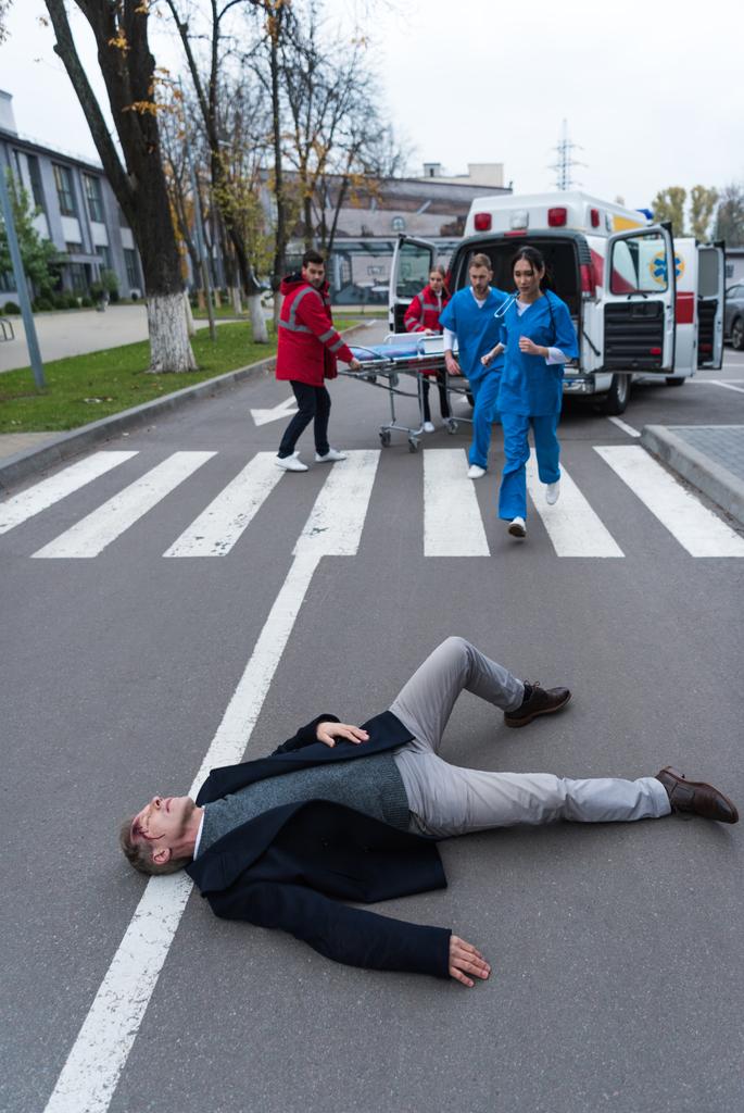 παραϊατρικό προσωπικό τρέχει να βοηθήσει το τραυματισμένο άνθρωπο που βρίσκεται σε έναν δρόμο  - Φωτογραφία, εικόνα
