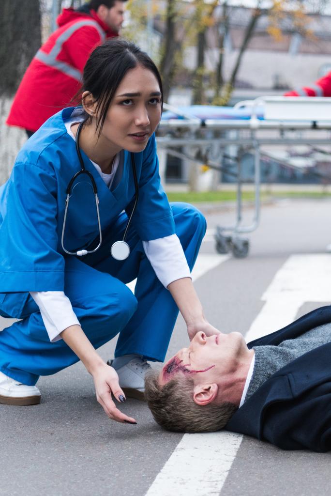 joven mujer asiática médico ayudar inconsciente lesionado hombre acostado en un calle
 - Foto, Imagen