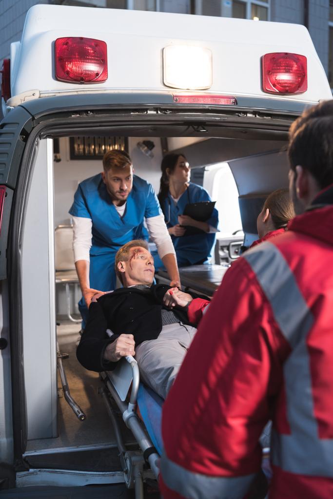 παραϊατρικό προσωπικό που κινείται τραυματισμένο άνθρωπο σε ασθενοφόρο - Φωτογραφία, εικόνα