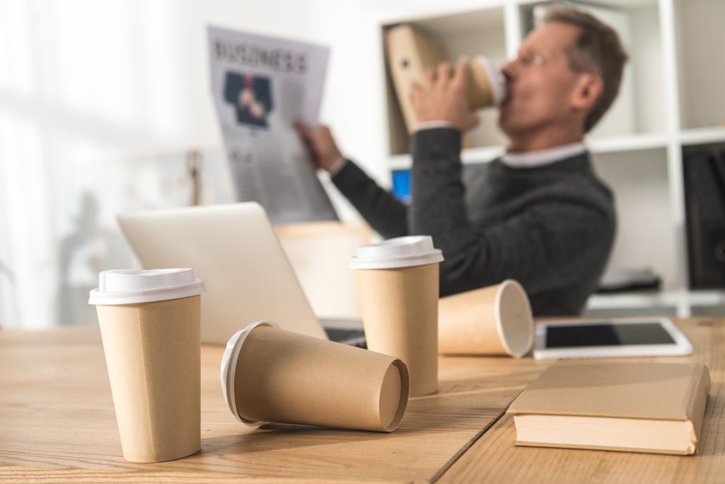 前景に散在の使い捨てのコーヒー カップでコーヒーを飲むビジネスマン - 写真・画像