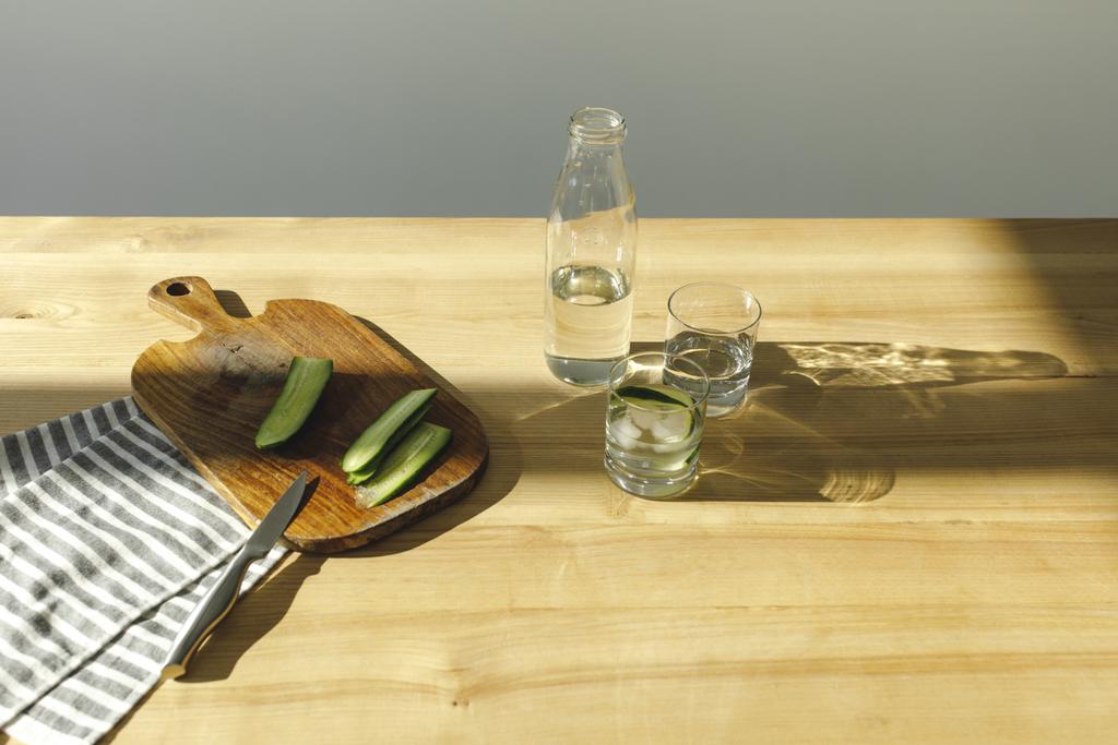 Blick auf geschnittene Gurken und Flasche mit Wasser auf Holztisch - Foto, Bild