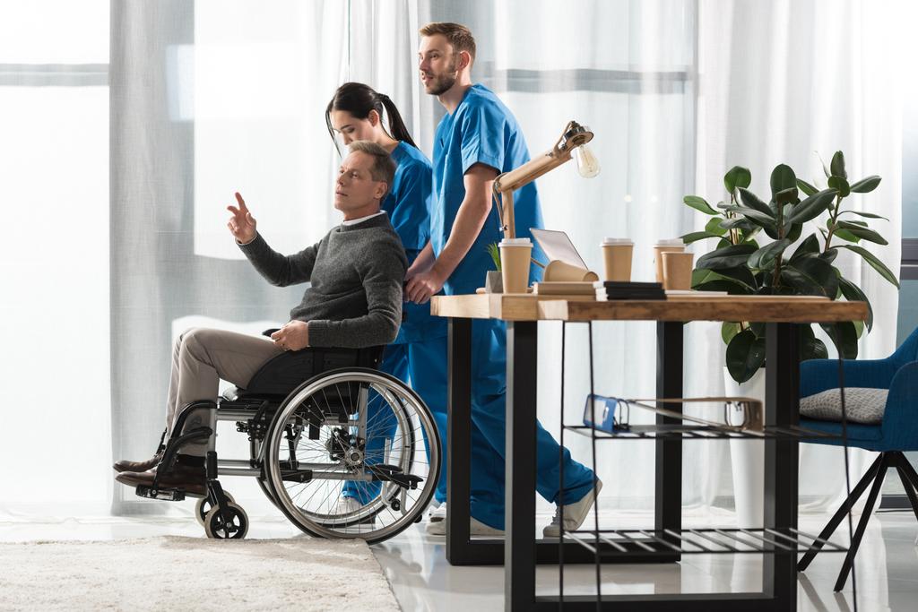 Медсестры помогают мужчине средних лет в инвалидном кресле
 - Фото, изображение