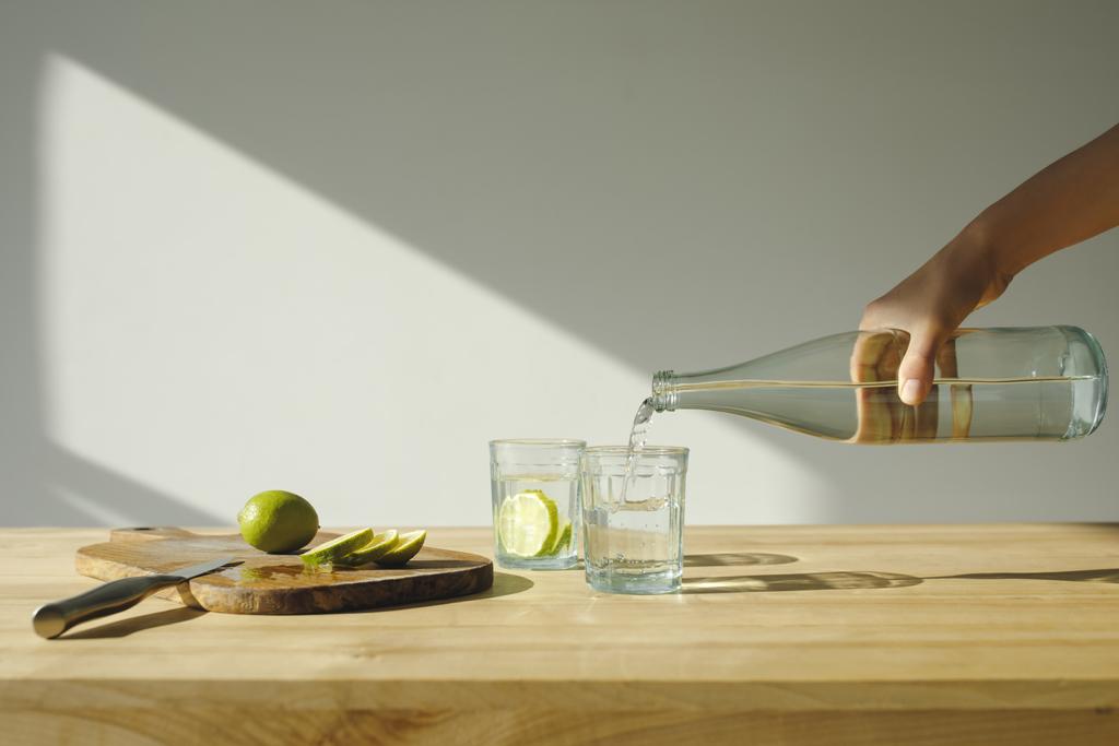περικομμένη εικόνα γυναίκα ρίχνει μεταλλικό νερό σε ποτήρι  - Φωτογραφία, εικόνα