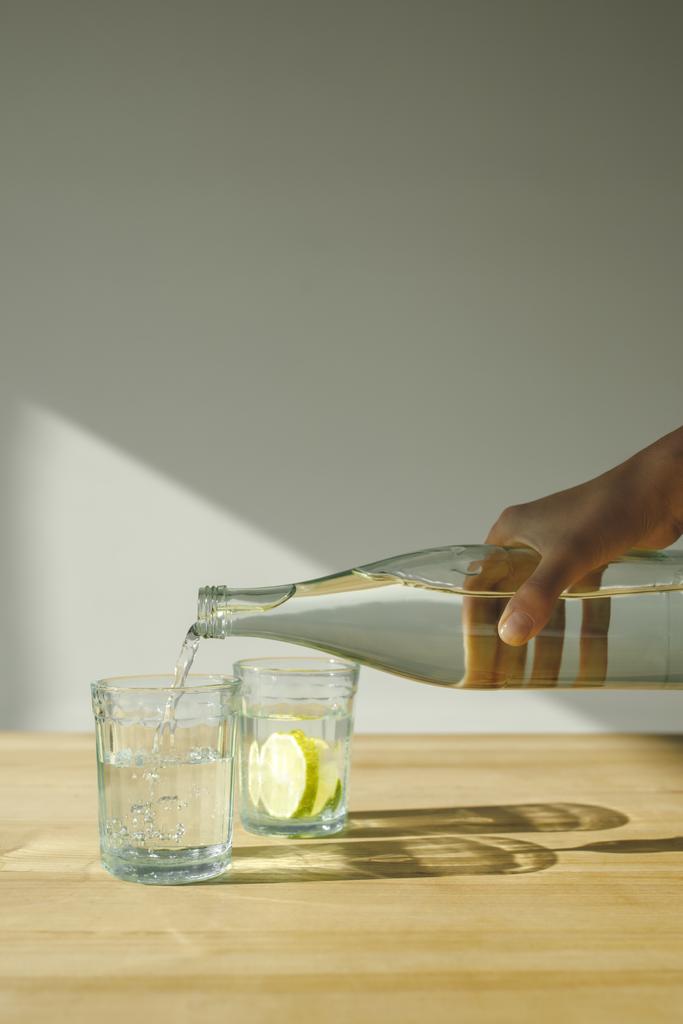abgeschnittenes Bild einer Frau, die Wasser aus Flasche in transparentes Glas gießt  - Foto, Bild