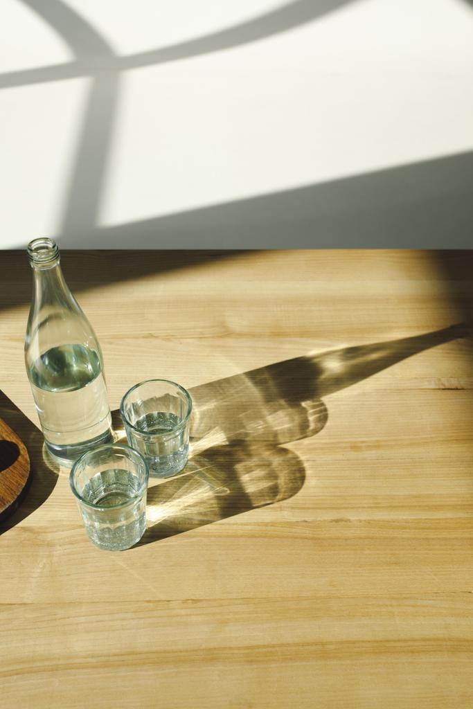 вид сверху на прозрачную бутылку и стаканы с минеральной водой
 - Фото, изображение