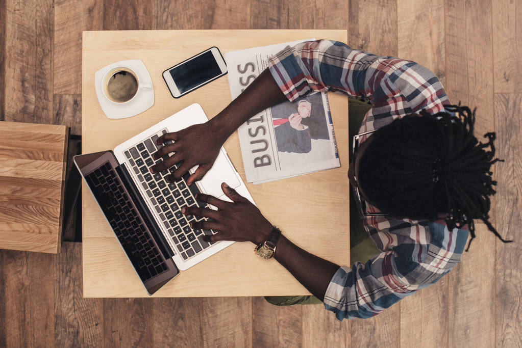 вид зверху афроамериканця з ноутбуком, смартфоном, чашкою кави та діловою газетою в кафе
 - Фото, зображення