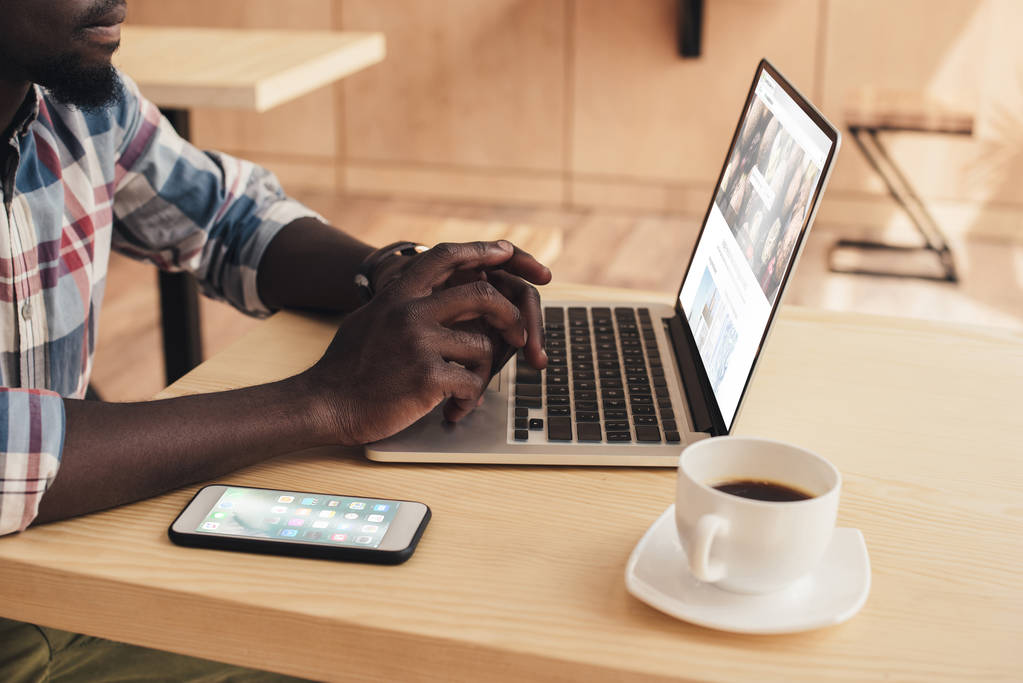 vista ritagliata dell'uomo afro-americano che utilizza il computer portatile con sito di foto di deposito in caffetteria
 - Foto, immagini