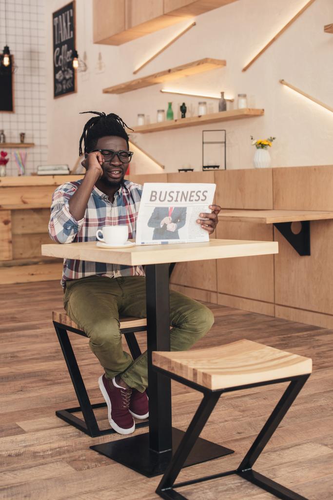 Afrikanisch-amerikanischer Mann spricht auf Smartphone, während er im Café Wirtschaftszeitung liest - Foto, Bild