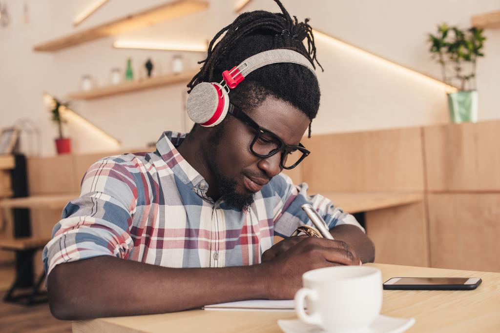 uomo afroamericano ascoltare musica e scrivere in blocco note in caffetteria
 - Foto, immagini
