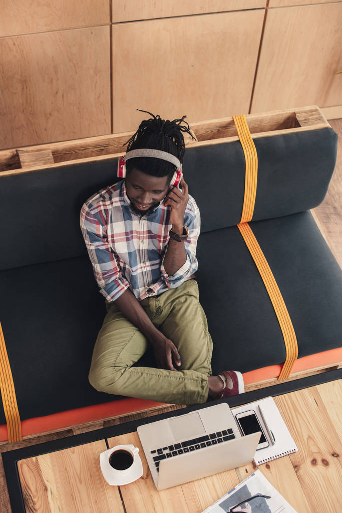 Overhead-Ansicht eines afrikanisch-amerikanischen Mannes, der mit Kopfhörern Musik hört und im Café Gadgets benutzt - Foto, Bild