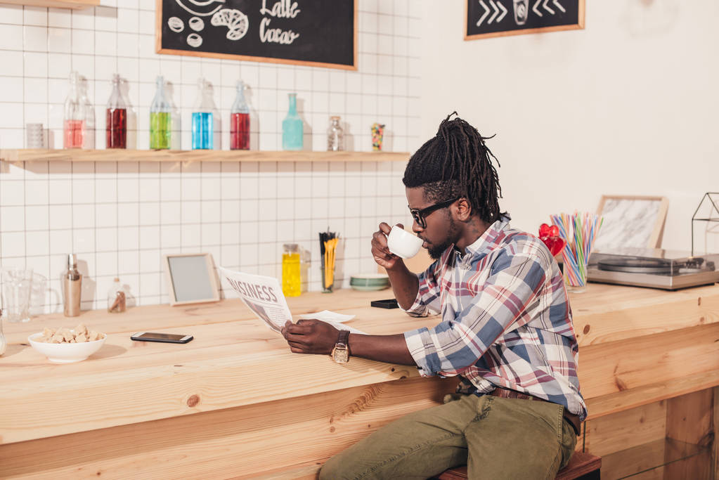 Afrikkalainen amerikkalainen mies juo kahvia ja lukee business sanomalehteä
 - Valokuva, kuva